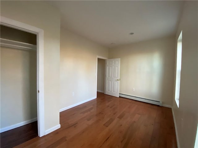 unfurnished bedroom with a closet, baseboard heating, and dark wood-type flooring