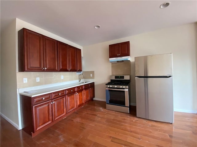 kitchen featuring appliances with stainless steel finishes, light wood-type flooring, backsplash, and sink