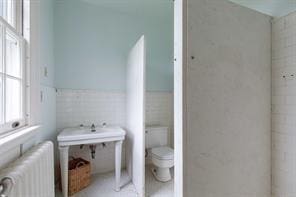 bathroom with toilet, tile walls, and radiator