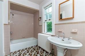 bathroom with sink, tile walls, radiator, and tiled shower / bath