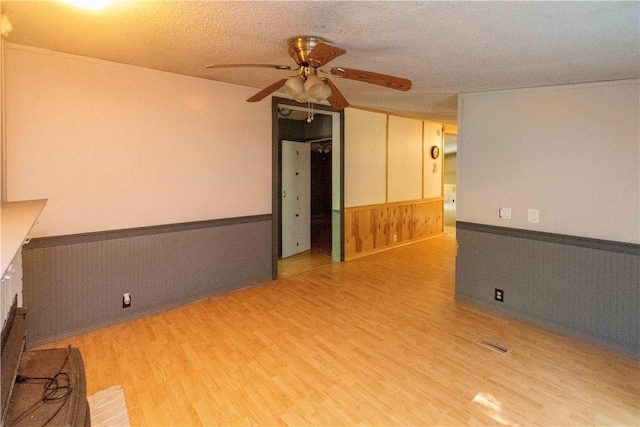 spare room featuring a brick fireplace, a textured ceiling, ceiling fan, wooden walls, and wood-type flooring