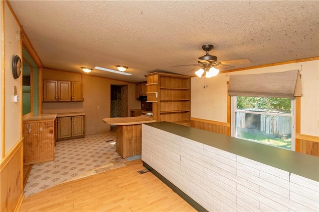 kitchen with kitchen peninsula, wooden walls, ceiling fan, and a textured ceiling