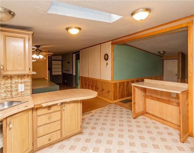 kitchen with kitchen peninsula, backsplash, a skylight, a textured ceiling, and ceiling fan