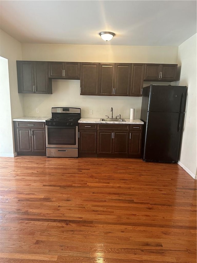 kitchen with black refrigerator, sink, hardwood / wood-style flooring, and stainless steel range oven