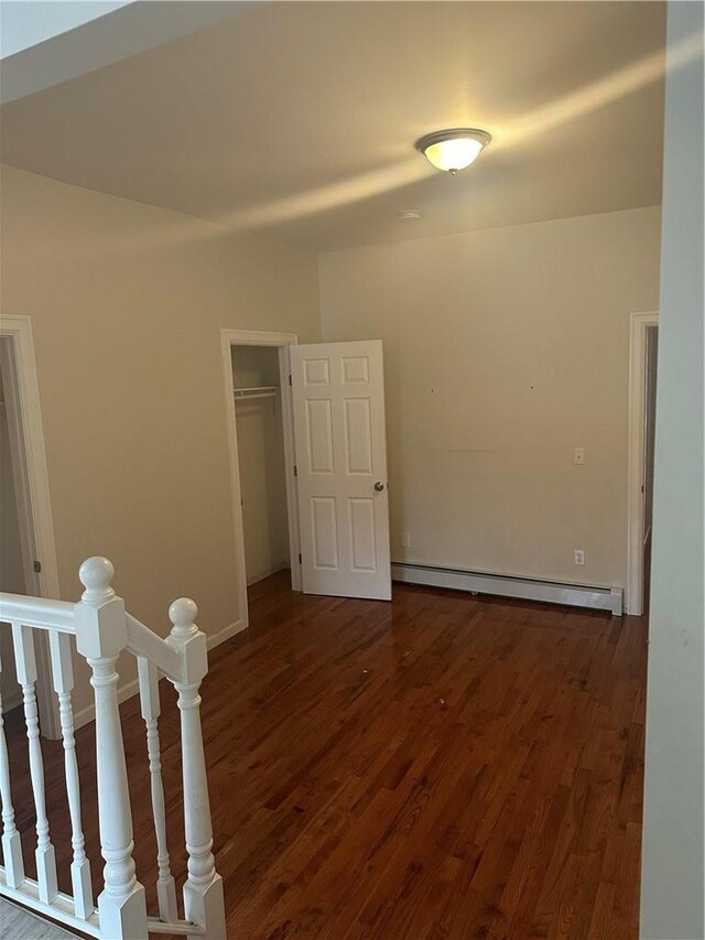 unfurnished bedroom with a walk in closet, dark hardwood / wood-style flooring, a baseboard radiator, and a closet