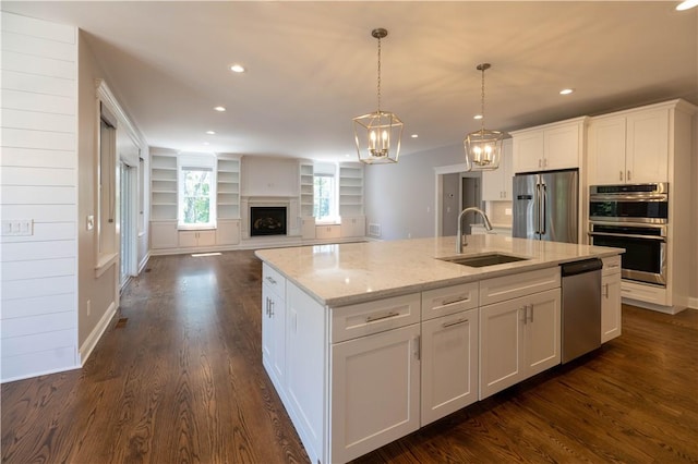 kitchen featuring sink, hanging light fixtures, stainless steel appliances, a center island with sink, and white cabinets