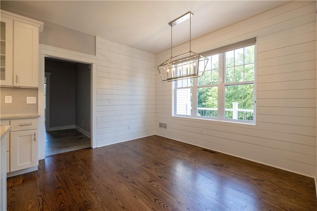 unfurnished dining area with dark hardwood / wood-style floors, plenty of natural light, and wooden walls