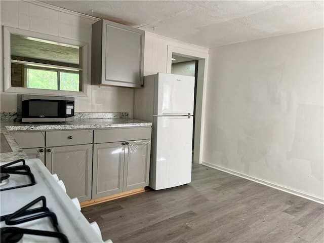 kitchen featuring freestanding refrigerator, stainless steel microwave, gray cabinets, wood finished floors, and a textured ceiling