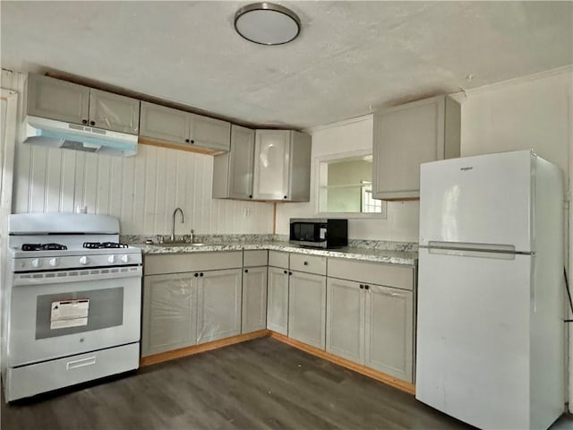 kitchen with white appliances, under cabinet range hood, dark wood finished floors, a sink, and light stone countertops
