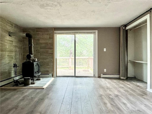 unfurnished living room featuring wood walls, light wood-type flooring, a wood stove, and baseboard heating