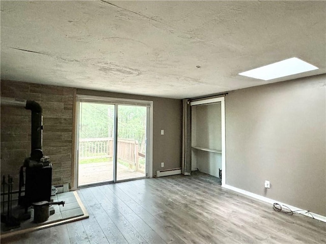 unfurnished living room with wood-type flooring, a skylight, a wood stove, and a baseboard heating unit