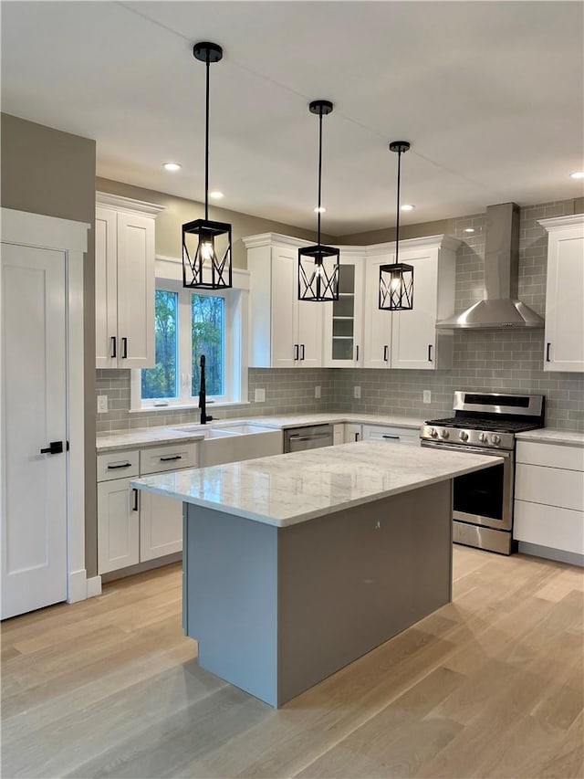 kitchen with wall chimney exhaust hood, stainless steel appliances, decorative light fixtures, white cabinets, and a center island