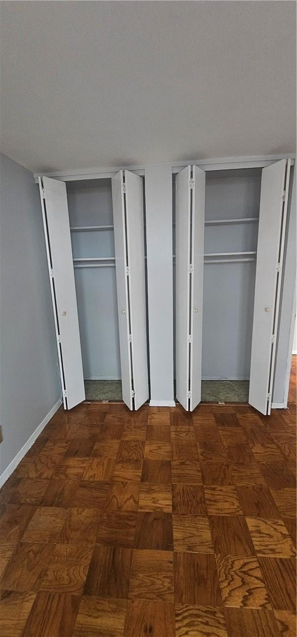 unfurnished bedroom featuring dark parquet floors and multiple closets