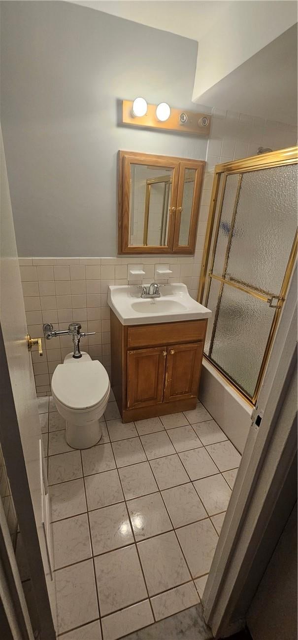 full bathroom with tile patterned flooring, combined bath / shower with glass door, toilet, vanity, and tile walls