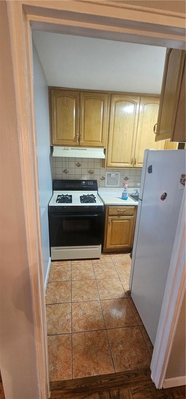 kitchen featuring tasteful backsplash, light brown cabinets, light tile patterned floors, range, and white fridge