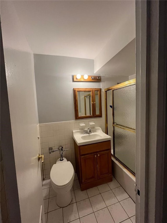 full bathroom featuring combined bath / shower with glass door, vanity, tile walls, tile patterned flooring, and toilet