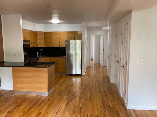 kitchen with decorative backsplash, black gas range oven, light hardwood / wood-style floors, kitchen peninsula, and stainless steel refrigerator