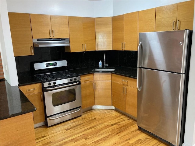 kitchen featuring sink, tasteful backsplash, dark stone countertops, appliances with stainless steel finishes, and light wood-type flooring