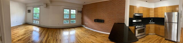 kitchen featuring appliances with stainless steel finishes, backsplash, light hardwood / wood-style flooring, and brick wall