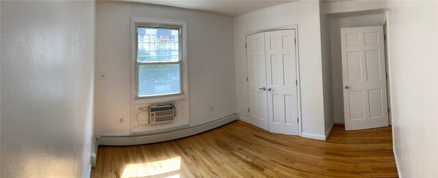 interior space with hardwood / wood-style flooring, a closet, a wall mounted AC, and a baseboard radiator