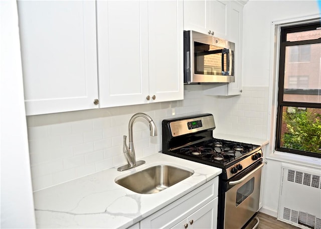 kitchen with radiator, sink, appliances with stainless steel finishes, light stone counters, and white cabinetry