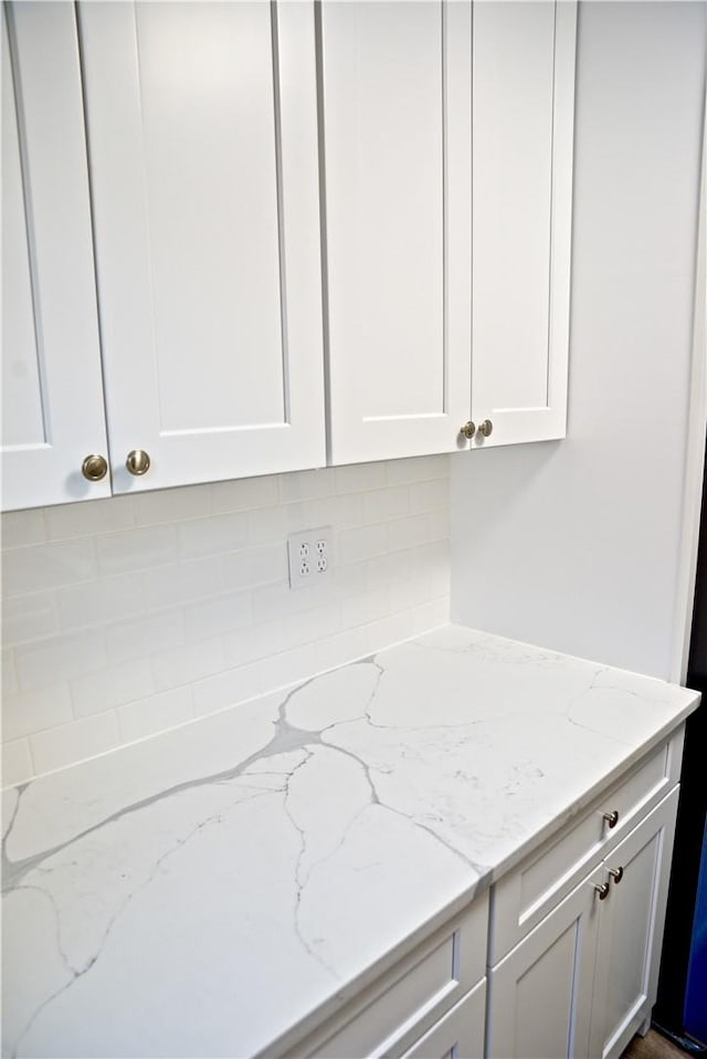 interior space featuring decorative backsplash, light stone counters, and white cabinetry