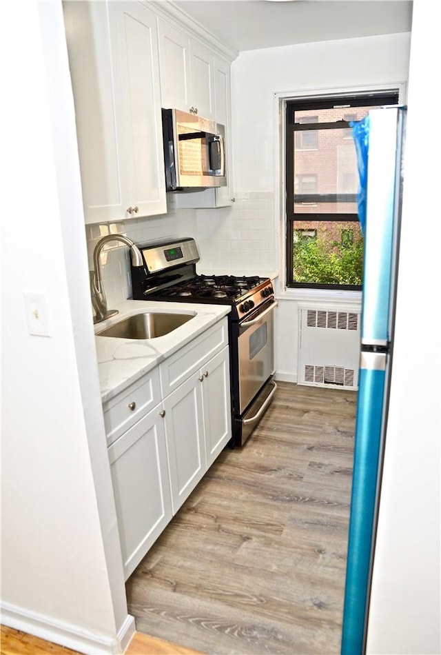 kitchen with sink, appliances with stainless steel finishes, light hardwood / wood-style floors, light stone counters, and white cabinetry