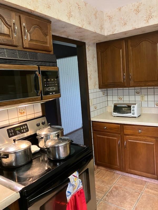 kitchen featuring electric range, light tile patterned floors, and tasteful backsplash