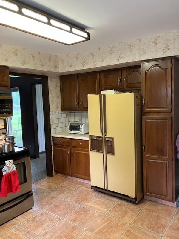 kitchen featuring white fridge with ice dispenser, electric stove, decorative backsplash, dark brown cabinets, and light tile patterned flooring