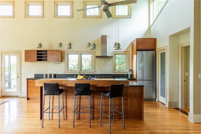 kitchen with a breakfast bar, stainless steel appliances, ceiling fan, and wall chimney exhaust hood