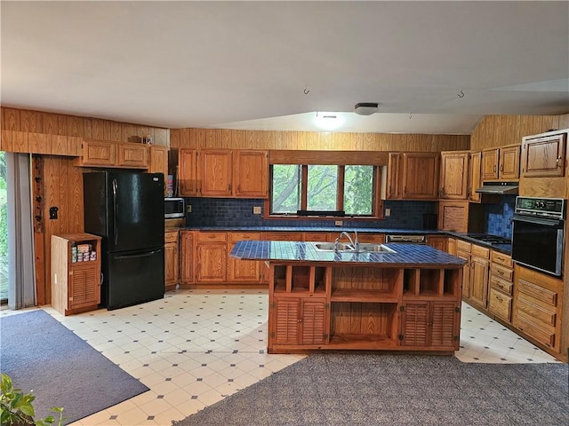 kitchen with black appliances, a center island with sink, sink, and vaulted ceiling