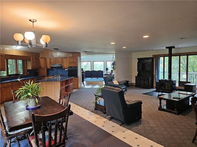 carpeted dining room featuring a wood stove, sink, and an inviting chandelier