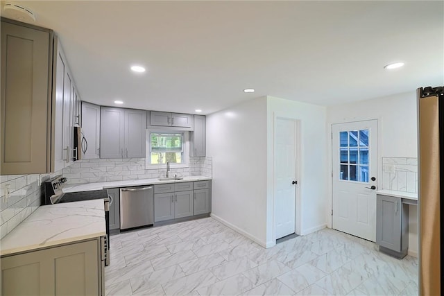 kitchen with gray cabinetry, sink, stainless steel appliances, light stone counters, and decorative backsplash