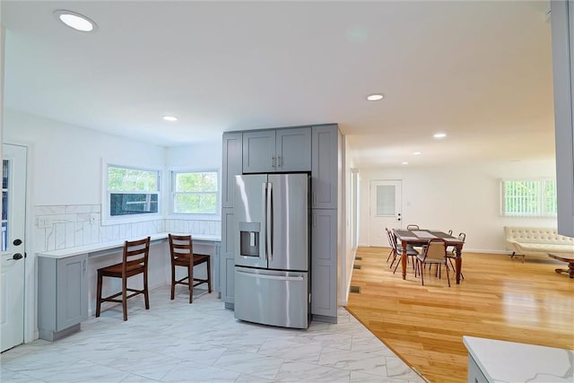 kitchen with backsplash, gray cabinets, light hardwood / wood-style flooring, and stainless steel refrigerator with ice dispenser