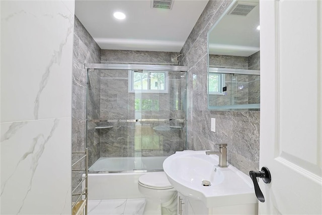 full bathroom featuring shower / bath combination with glass door, vanity, toilet, and tile walls