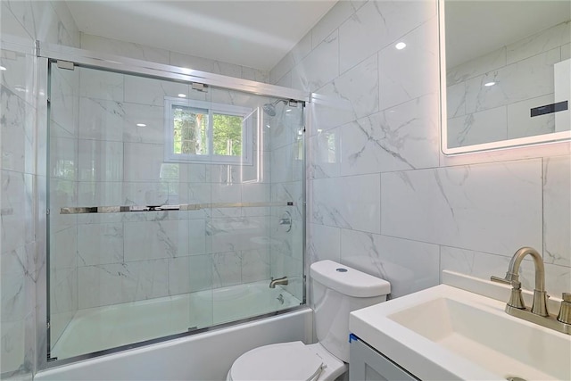 full bathroom with combined bath / shower with glass door, vanity, toilet, and tile walls