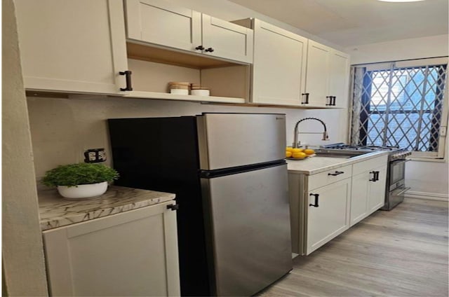 kitchen with white cabinets, stainless steel fridge, light wood-type flooring, and sink