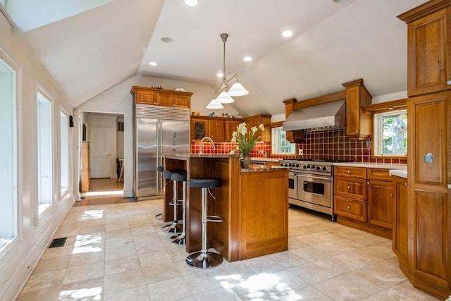 kitchen featuring wall chimney exhaust hood, tasteful backsplash, an island with sink, a kitchen bar, and high quality appliances