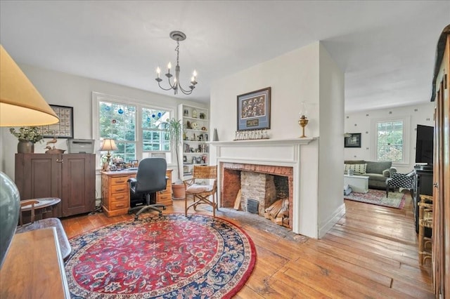 office space with light hardwood / wood-style floors, an inviting chandelier, and a brick fireplace