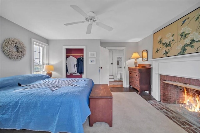 carpeted bedroom featuring a brick fireplace, a closet, a spacious closet, and ceiling fan