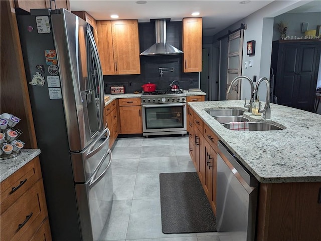 kitchen featuring light stone countertops, sink, stainless steel appliances, wall chimney range hood, and a barn door