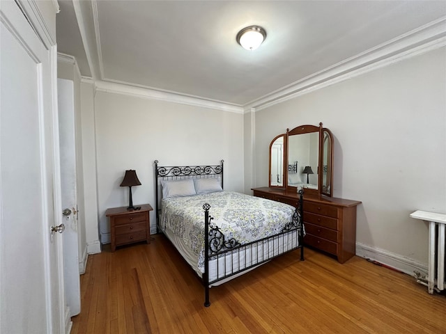 bedroom with ornamental molding and wood finished floors