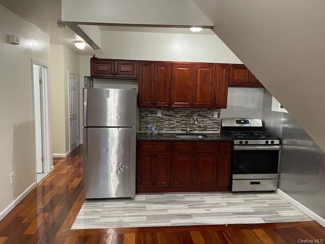 kitchen featuring dark stone counters, sink, light wood-type flooring, appliances with stainless steel finishes, and tasteful backsplash