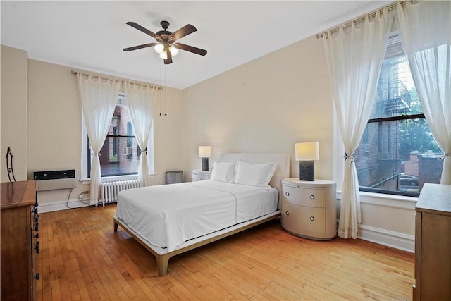 bedroom featuring light wood-type flooring, radiator heating unit, baseboards, and a ceiling fan