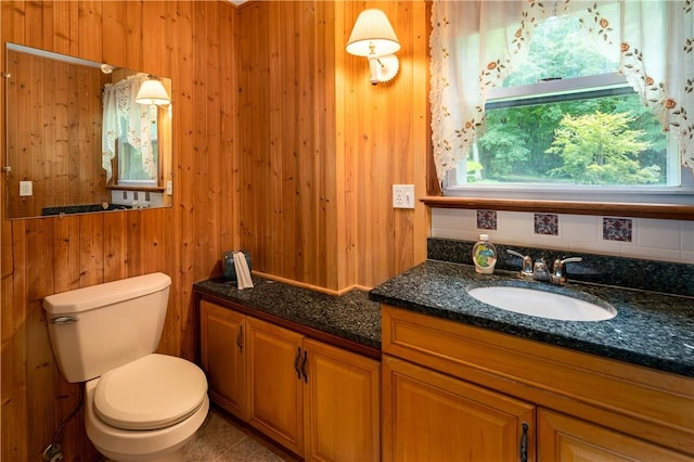 bathroom with vanity, toilet, and wood walls