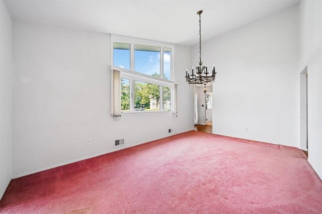 carpeted spare room with a towering ceiling and an inviting chandelier