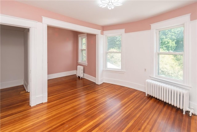 unfurnished bedroom featuring radiator heating unit, dark hardwood / wood-style floors, and multiple windows