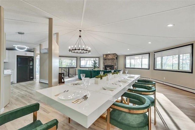 dining space featuring an inviting chandelier, a stone fireplace, baseboard heating, and light hardwood / wood-style flooring