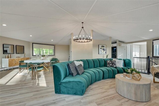 living room with a notable chandelier, lofted ceiling, an AC wall unit, and light hardwood / wood-style flooring