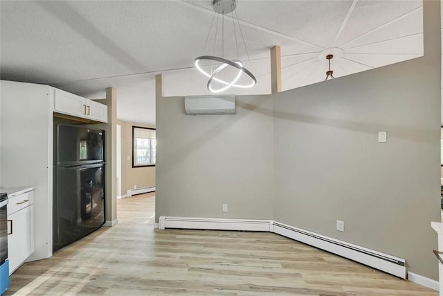 kitchen with pendant lighting, black refrigerator, light hardwood / wood-style flooring, a wall mounted AC, and white cabinetry